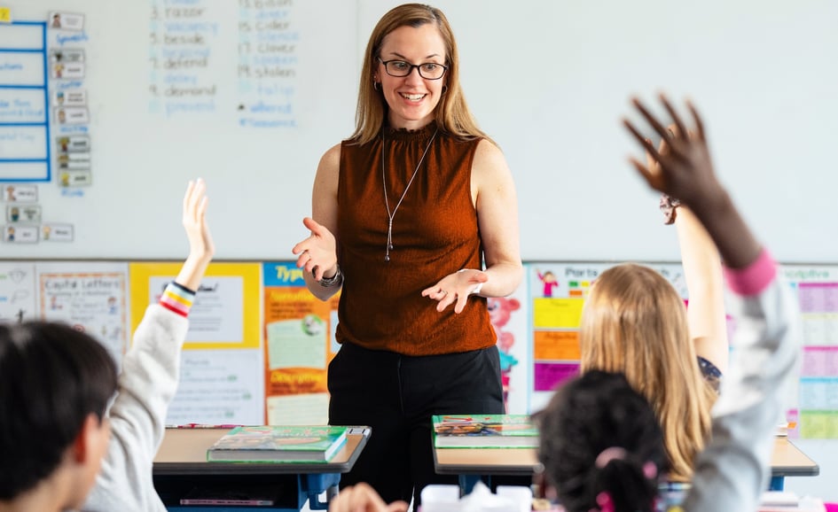 Female teacher in front of classroom with students hand raised