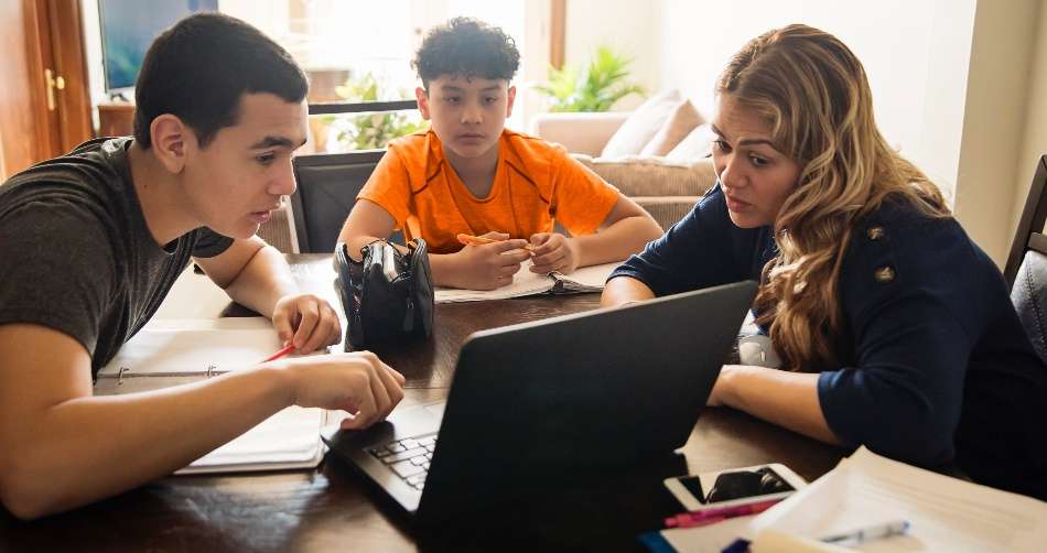 Adult female tutor at table and computer with two male students