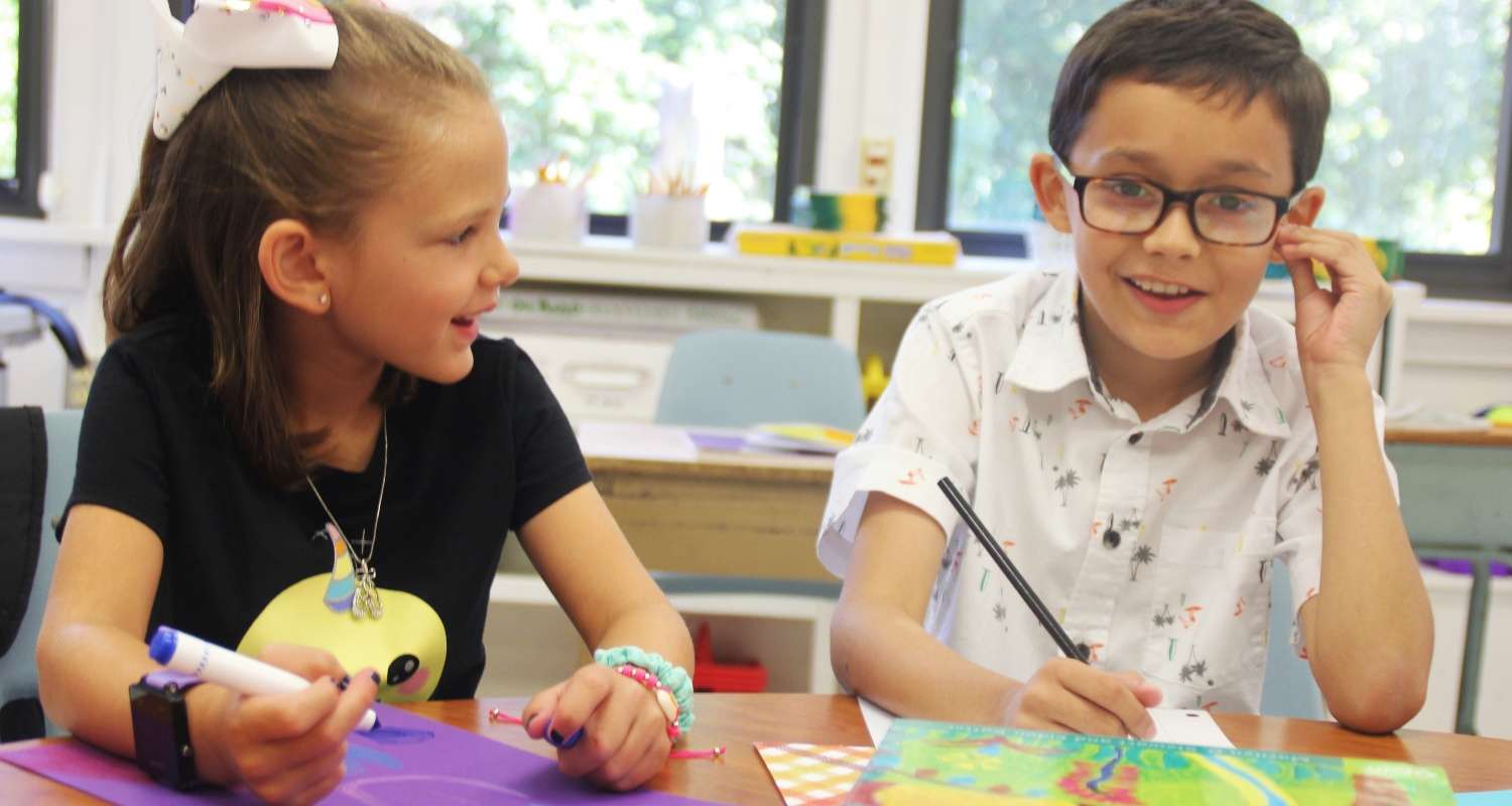 two elementary students working at table smiling