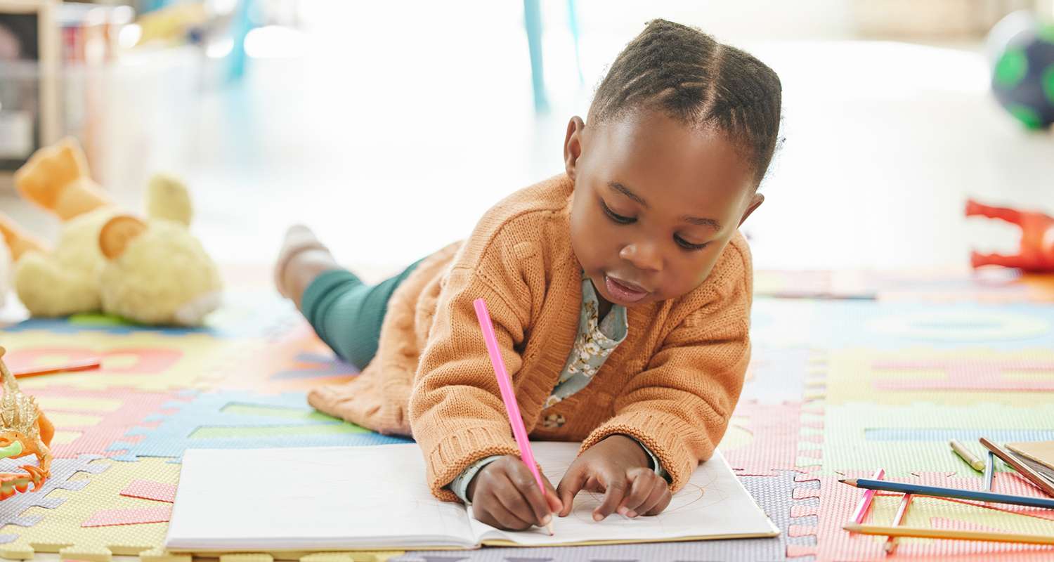 Preschool-girl-lying-on-her-stomach-drawing-on-some-paper