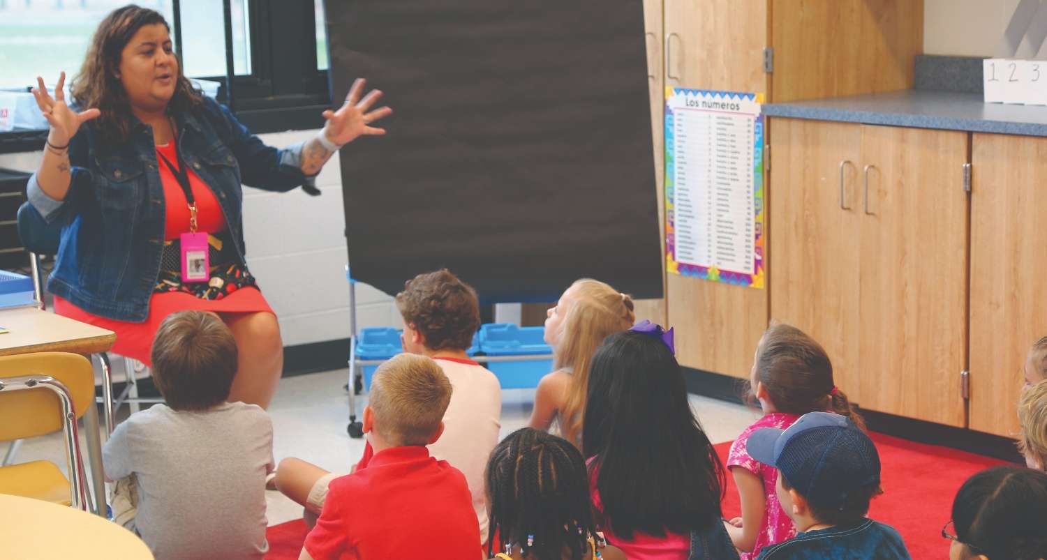 Teacher talking with elementary students seated on floor