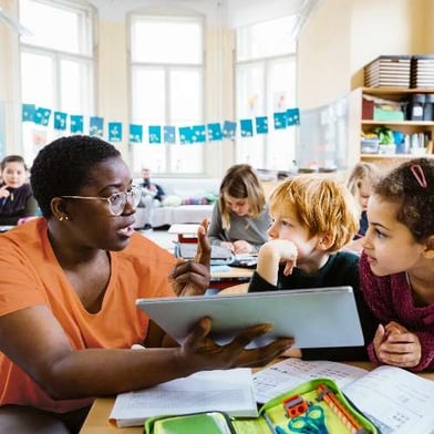 teacher showing students tablet at desk
