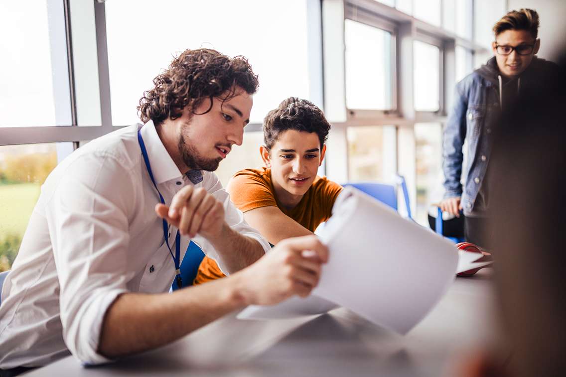 Teacher-at-a-table-showing-papers-to-a-teenage-student